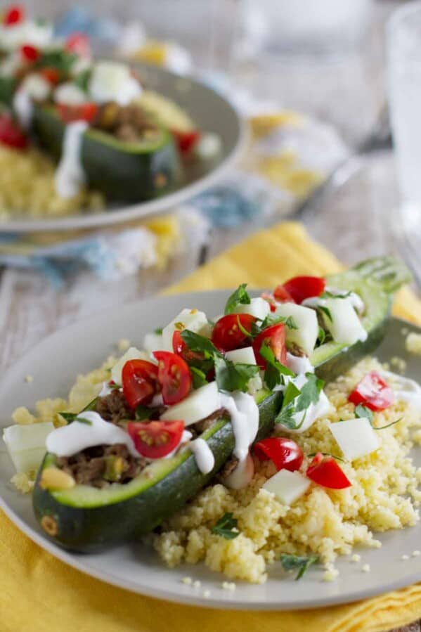 Zucchini boat topped with yogurt and tomatoes on top of a bed of couscous