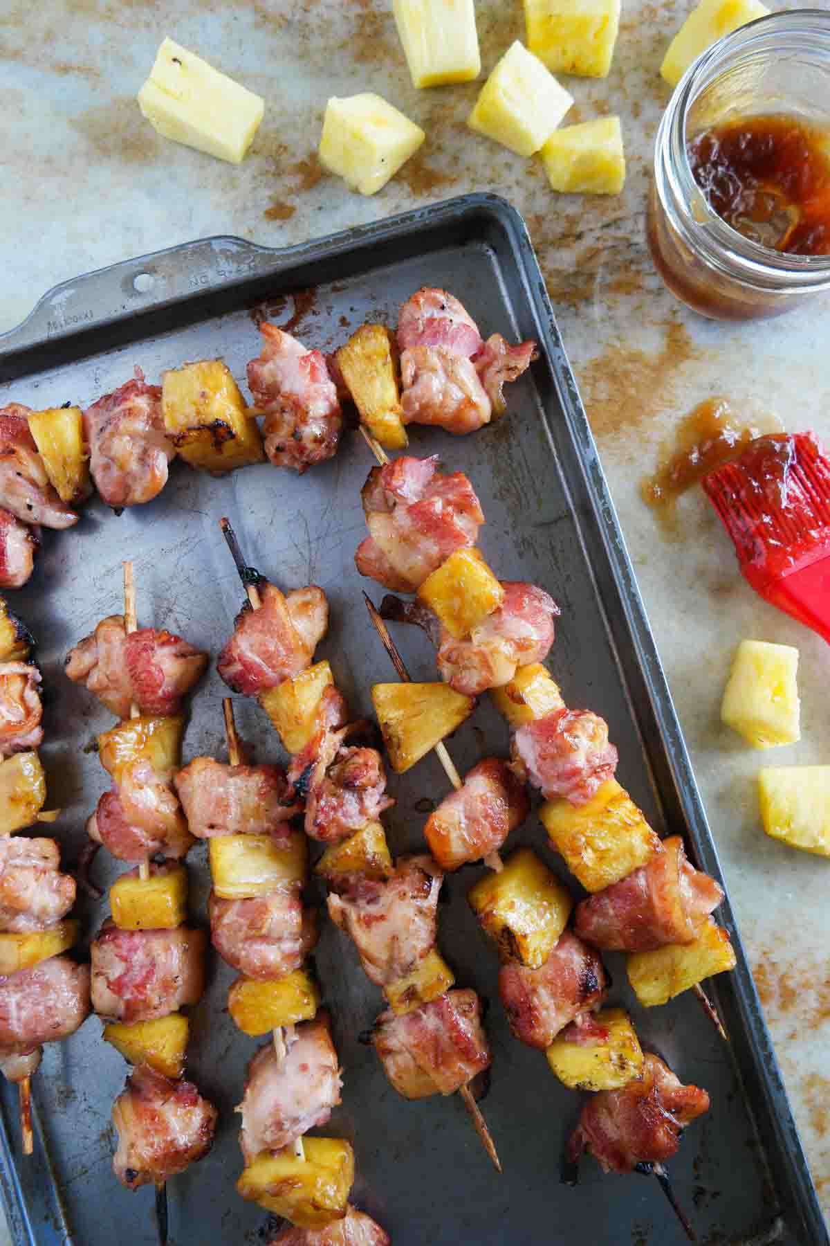 overhead view of skewers with bacon wrapped chicken and pineapple with teriyaki sauce