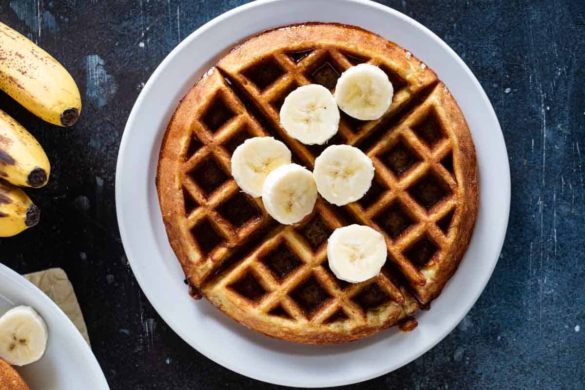 Banana waffle on a plate with fresh bananas on top.