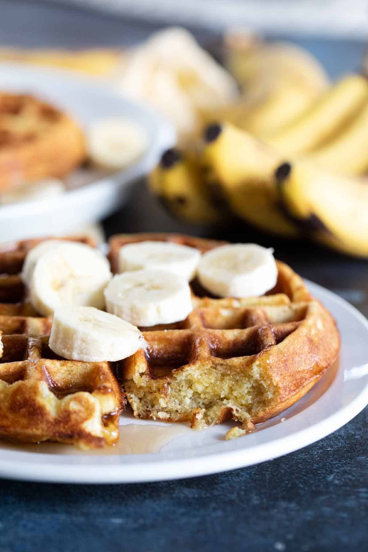 Banana Waffle topped with fresh bananas with a bite taken from it to show texture