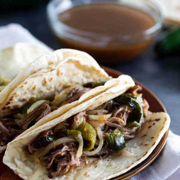 3 brisket tacos with peppers and onions with dipping broth.