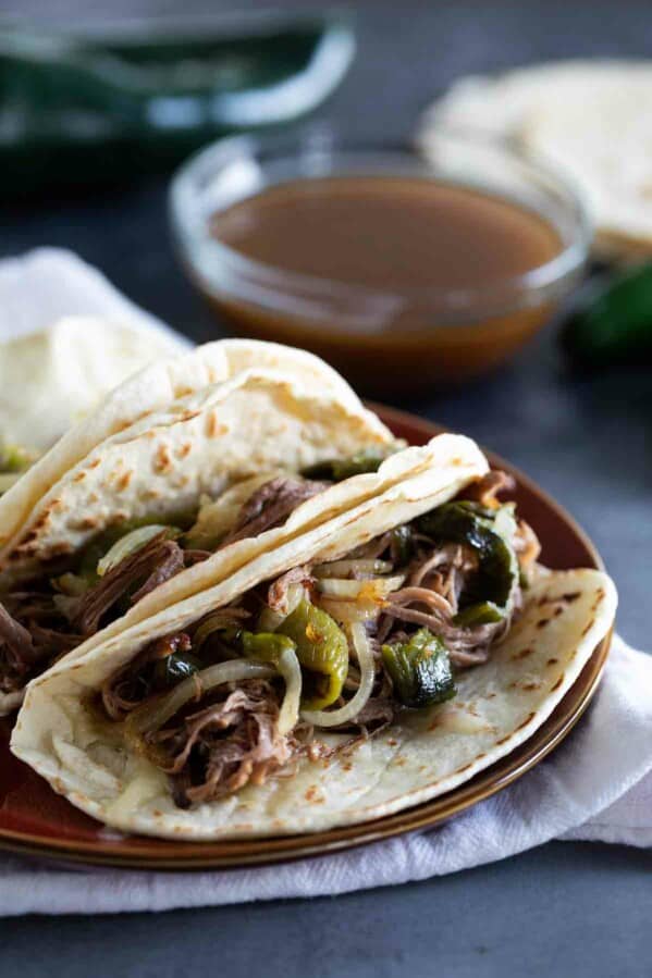 3 brisket tacos with peppers and onions with dipping broth.