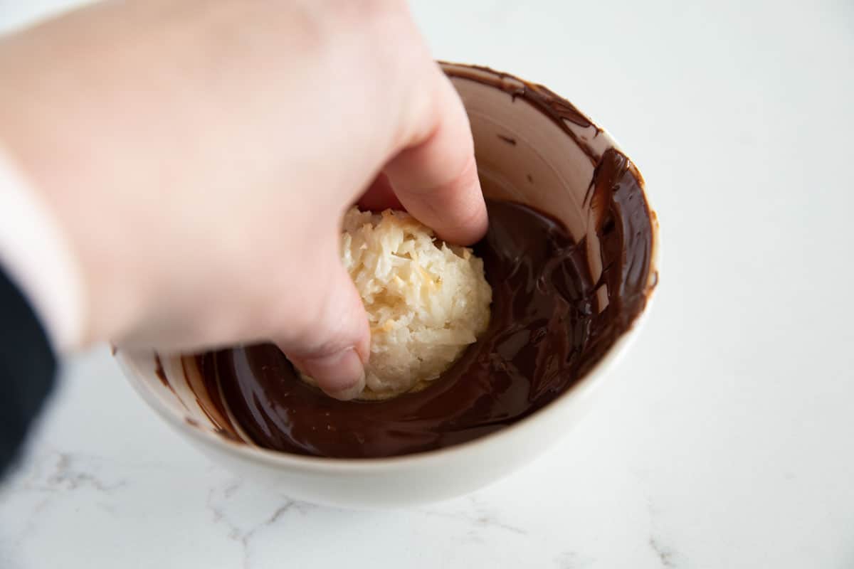 Lightly crispy on the outside and chewy on the inside, these Coconut Macaroons are made for coconut lovers! Dip the bottoms in chocolate for an even more decadent treat. dipping a coconut macaroon in chocolate