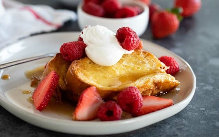 plate with Creme Brulee French Toast topped with berries and whipped cream.