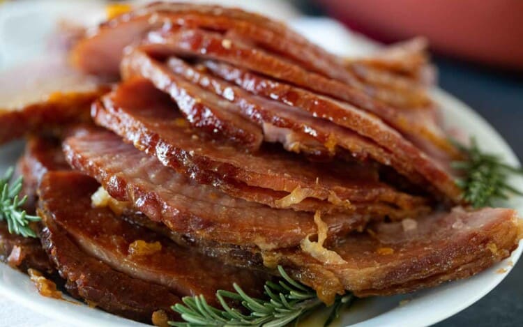 slices of Crock Pot Ham on a plate with fresh rosemary