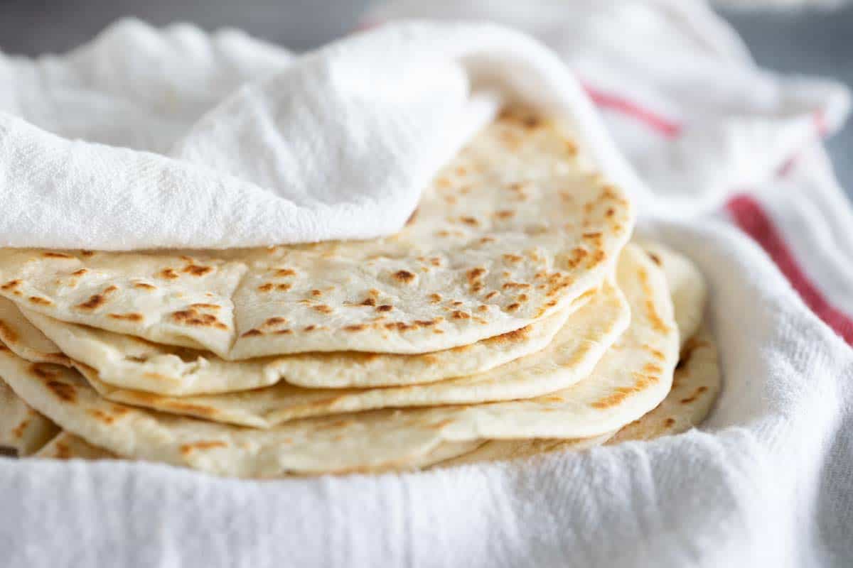 homemade flour tortillas stacked on each other under a white towel.