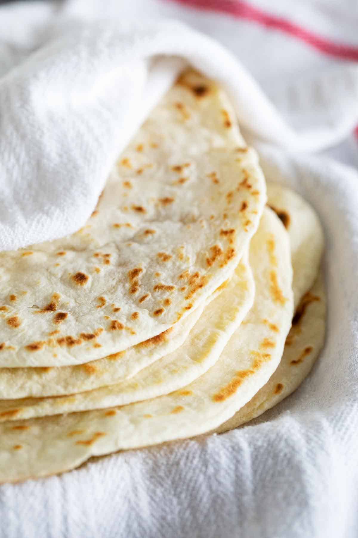 stack of homemade flour tortillas wrapped in a towel.
