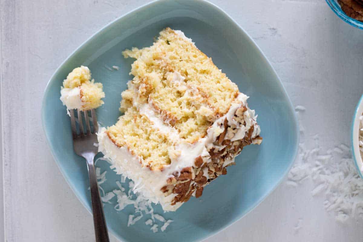 slice of Italian Cream Cake on a blue plate with a forkful taken