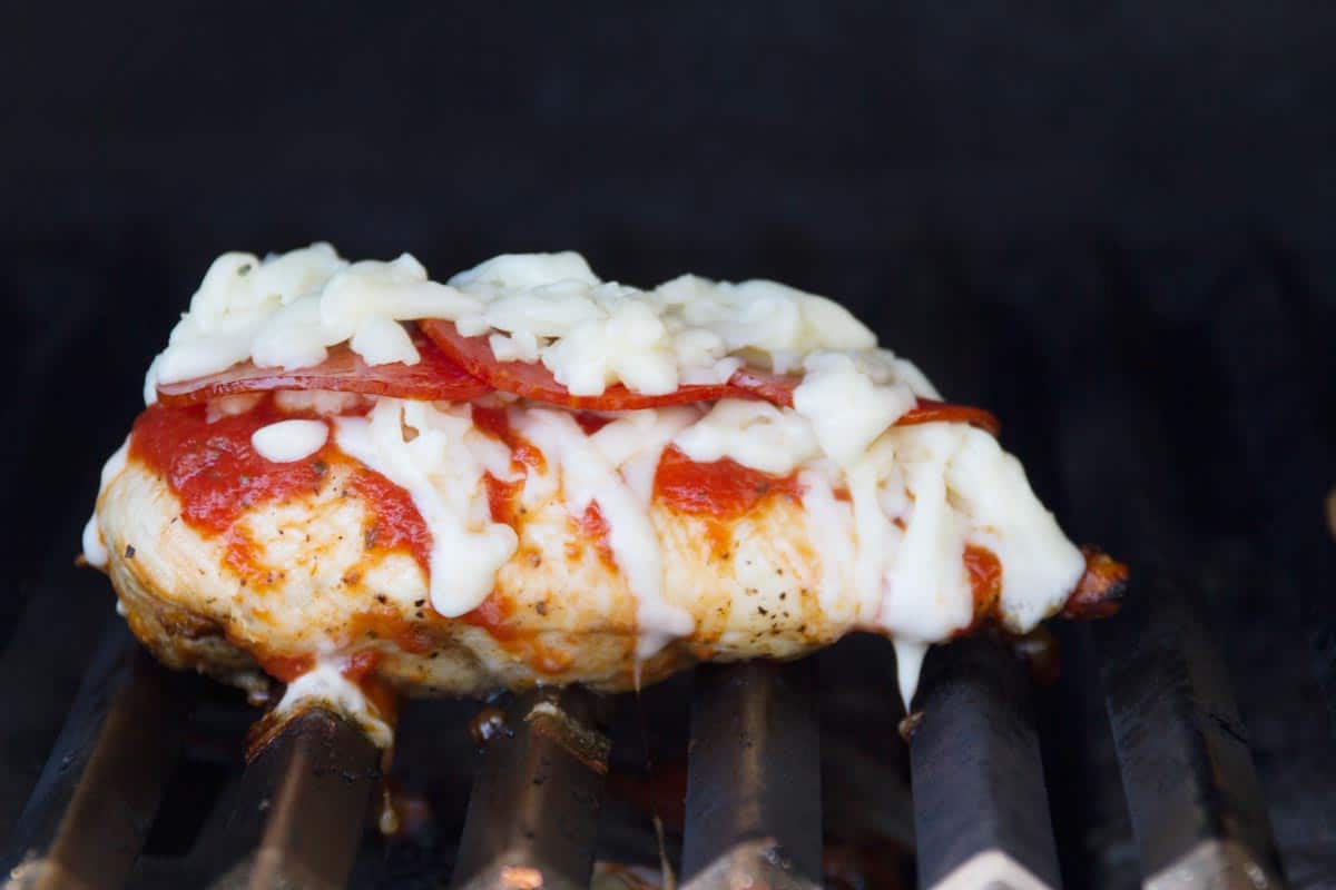 Chicken breast on a grill topped with pizza sauce, pepperoni, and cheese