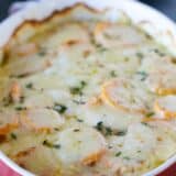 full dish of scalloped sweet potatoes topped with fresh thyme