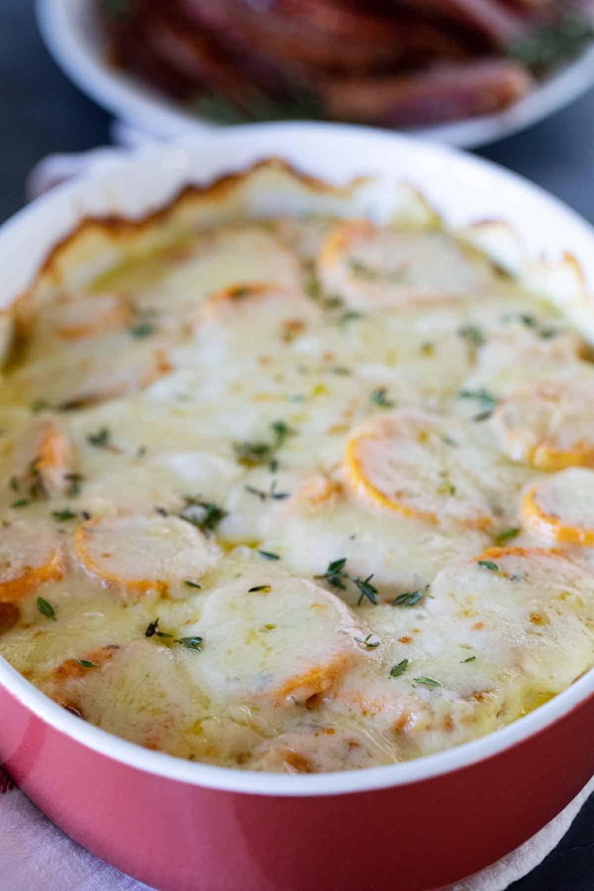 full dish of scalloped sweet potatoes topped with fresh thyme