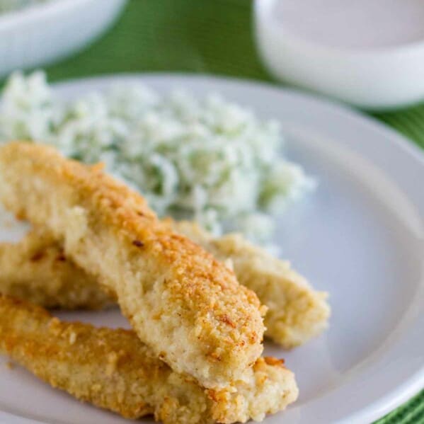 Tortilla Crusted Chicken Tenders on a plate with dipping sauce in the background.