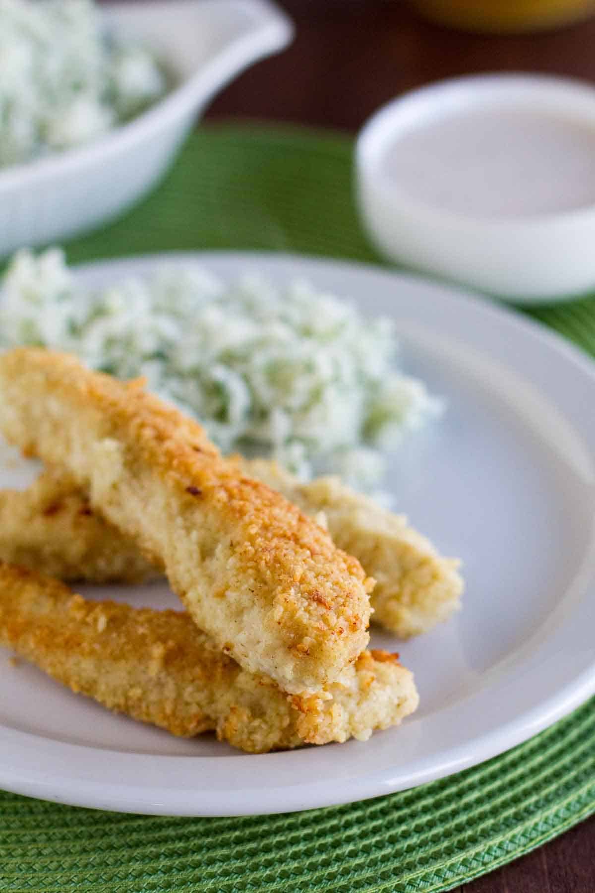 Tortilla Crusted Chicken Tenders on a plate with dipping sauce in the background.