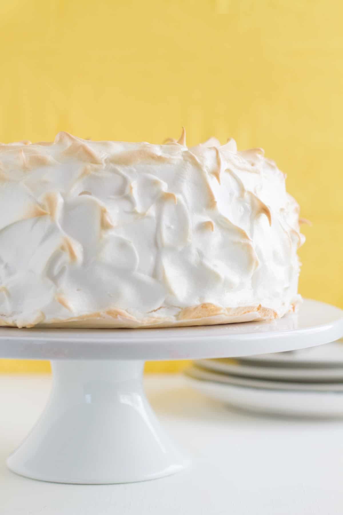 full Lemon Meringue Angel Cake on a cake stand with yellow in the background