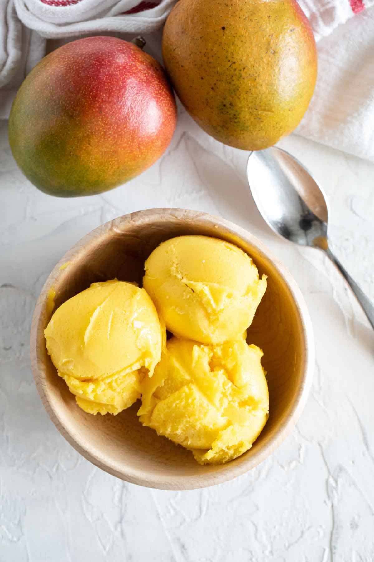 Mango sorbet in a bowl with fresh mangoes behind