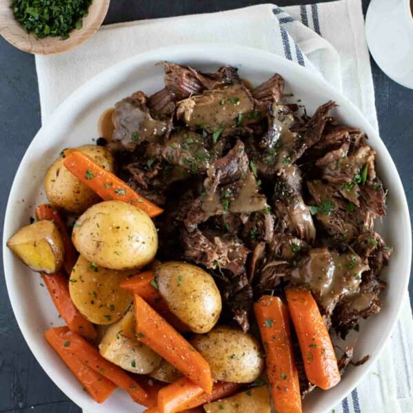 Serving plate with chunks of pot roast with gravy and carrots and potatoes