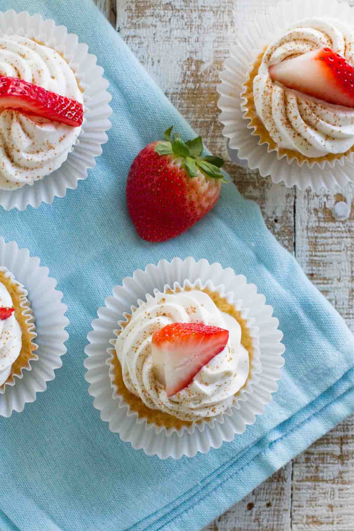 Tres Leches Cupcakes on a blue napkin with strawberries