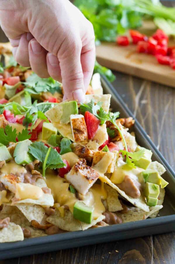 hand with a chip filled with nacho toppings