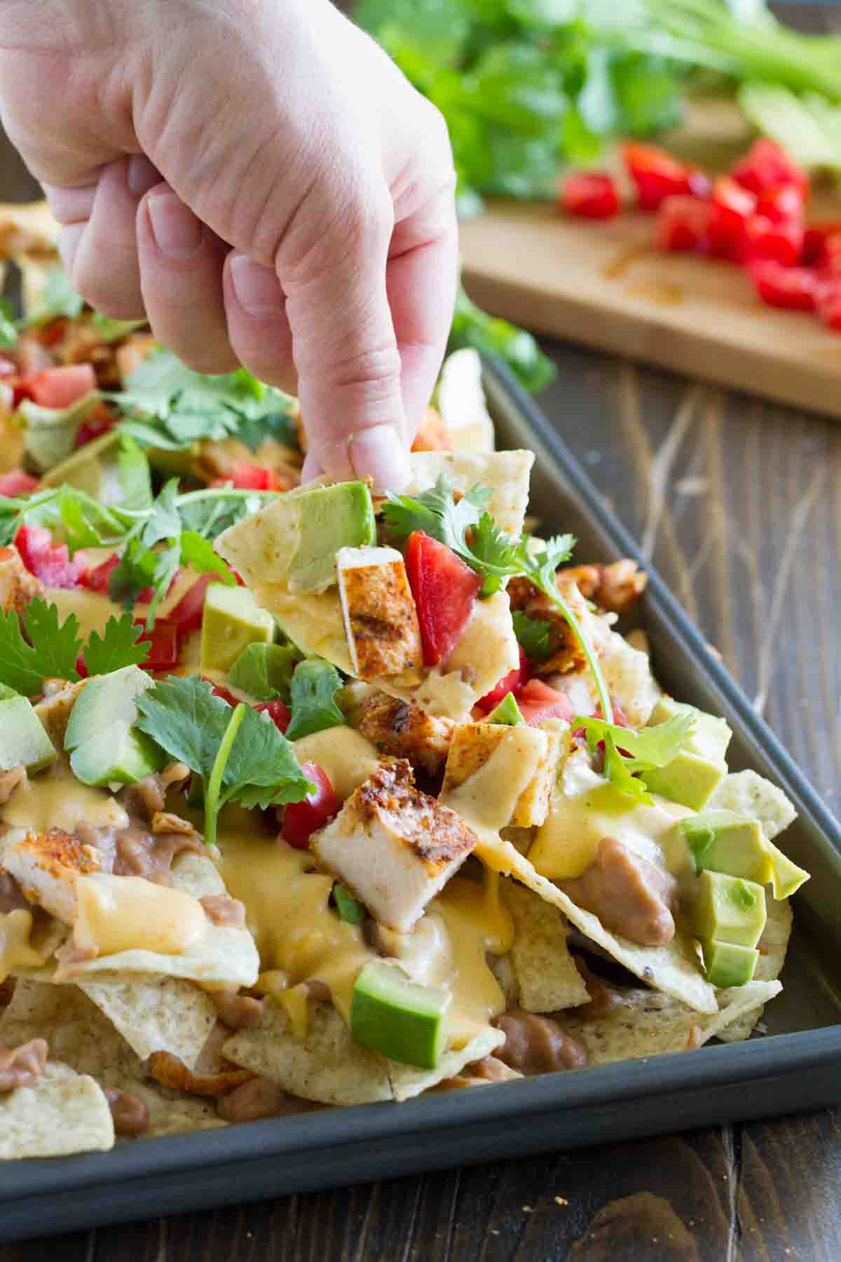 hand with a chip filled with nacho toppings