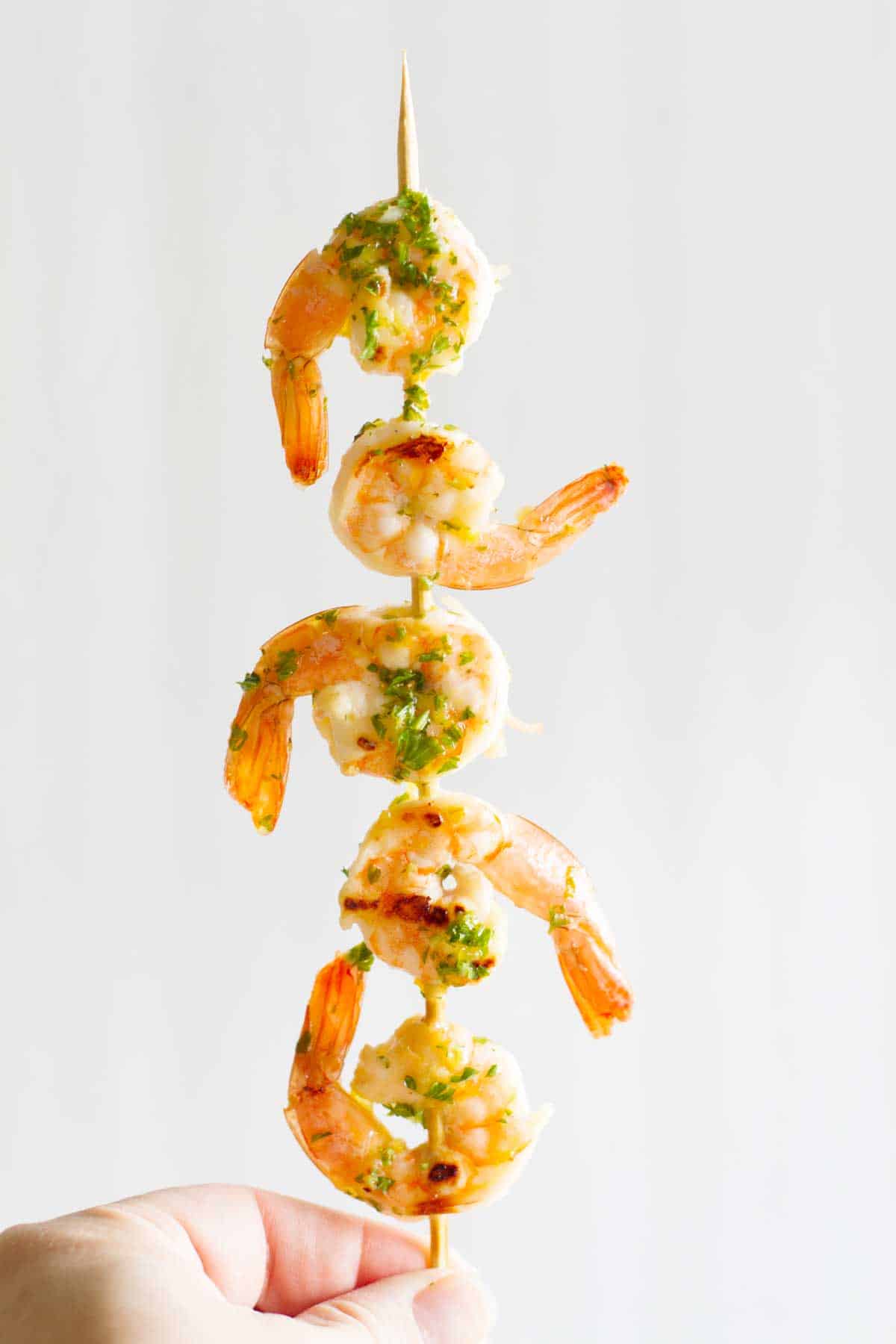 Hand holding grilled lemon shrimp.