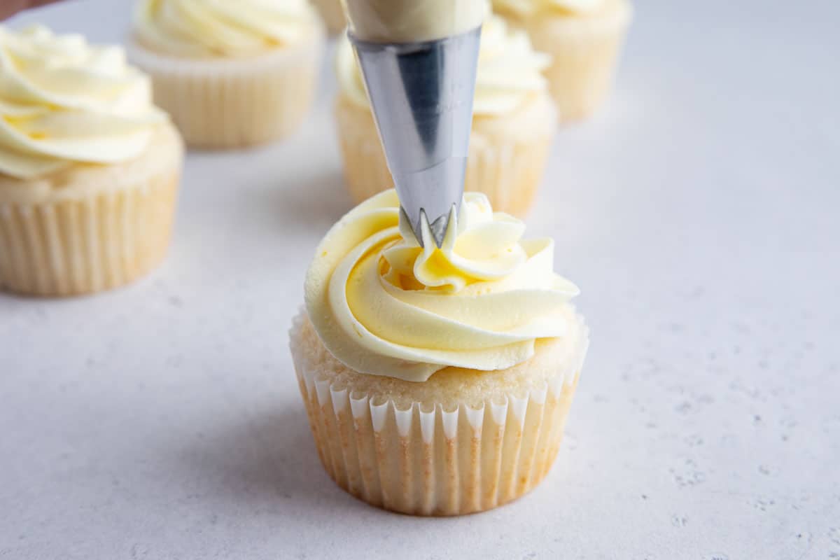 piping lemon buttercream onto a cupcake