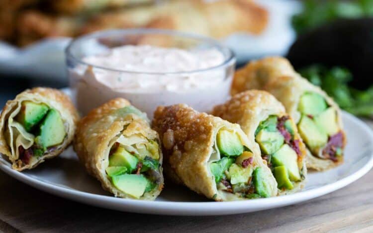 Avocado egg rolls on a plate with chipotle ranch dipping sauce in the background