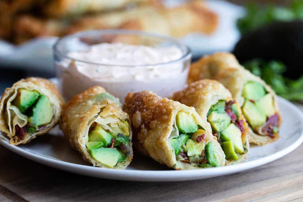 Avocado egg rolls on a plate with chipotle ranch dipping sauce in the background