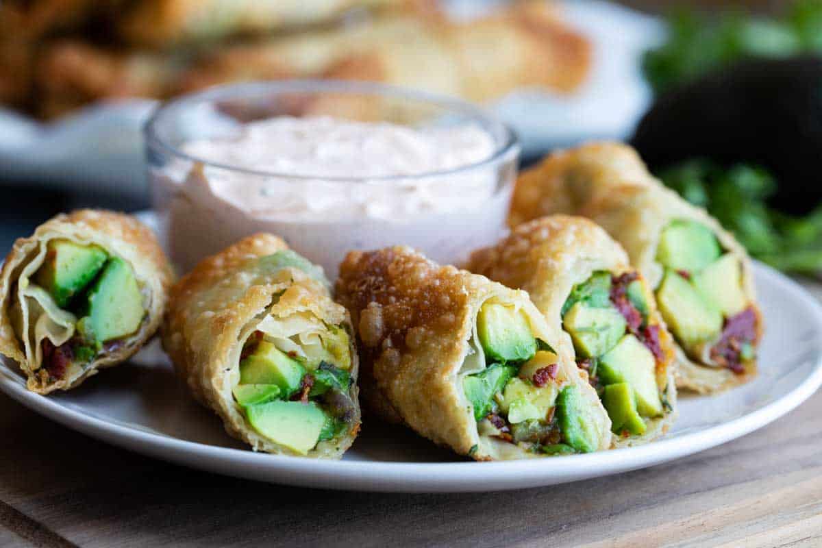 A riff on the popular restaurant appetizer, these Avocado Egg Rolls with Chipotle Ranch Dipping Sauce are easy to make at home and just as good! Avocado egg rolls on a plate with chipotle ranch dipping sauce in the background