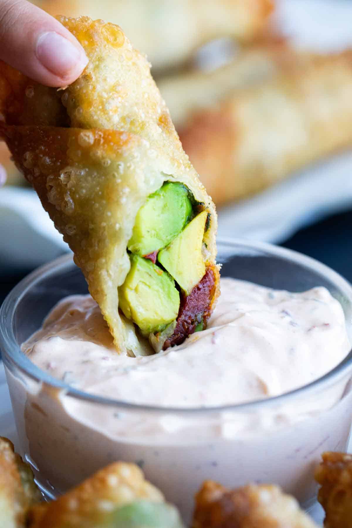 dipping an avocado egg roll into chipotle ranch dipping sauce.