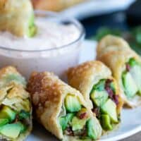 Avocado egg rolls cut in half on a plate with chipotle ranch dipping sauce.