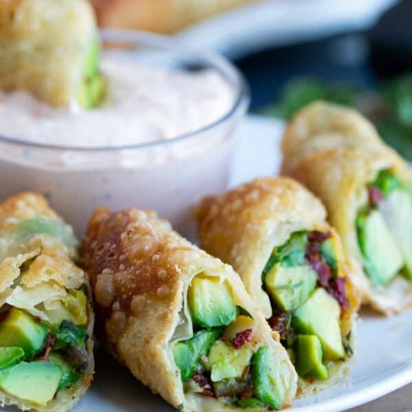 Avocado egg rolls cut in half on a plate with chipotle ranch dipping sauce.