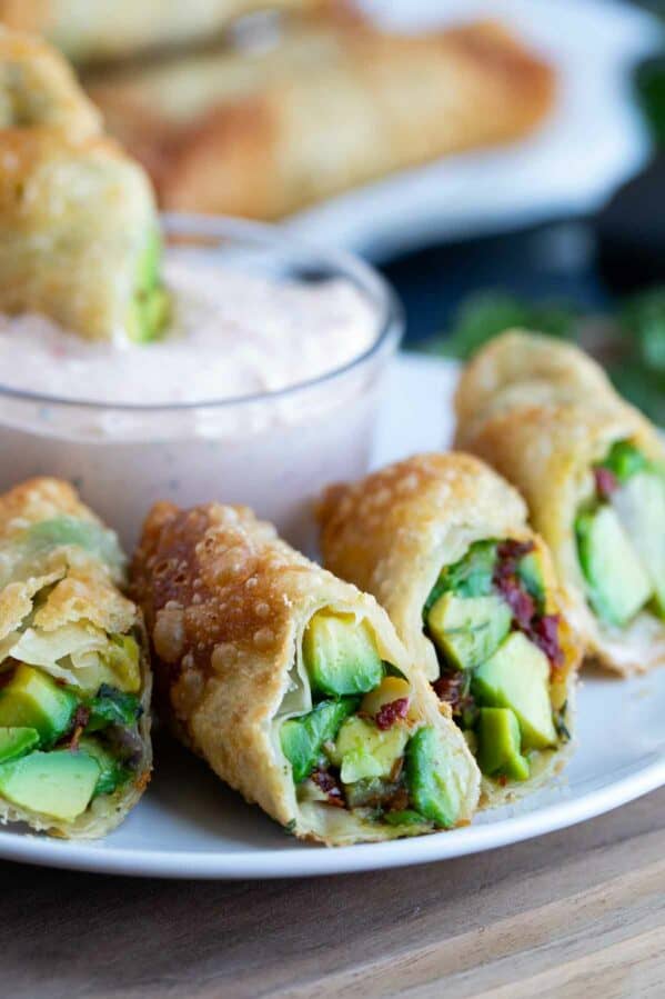 Avocado egg rolls cut in half on a plate with chipotle ranch dipping sauce.