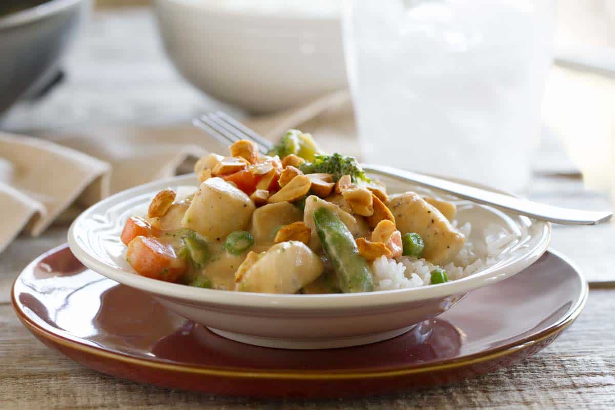 Bowl with a serving of peanut chicken stir fry topped with chopped peanuts