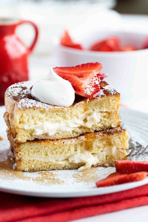 Stuffed French Toast cut and stacked topped with strawberries, whipped cream, and powdered sugar