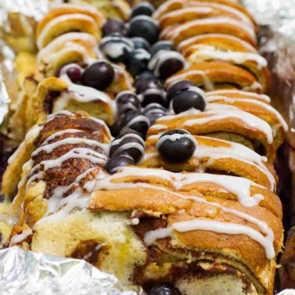 loaf of campfire cinnamon blueberry bread in foil topped with blueberries and glaze