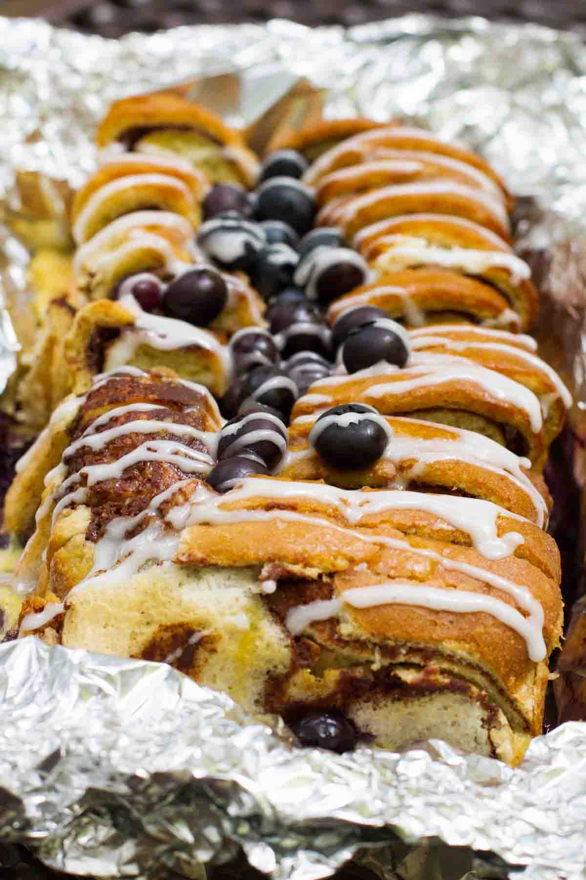 loaf of campfire cinnamon blueberry bread in foil topped with blueberries and glaze