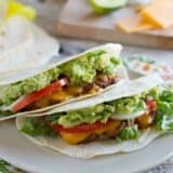 two Cheeseburger Tacos on a plate with toppings in the background