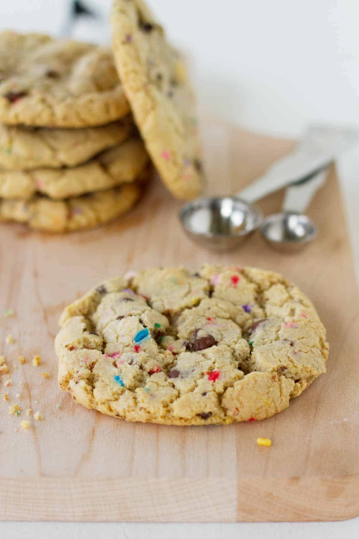 These Chocolate Chip Sprinkle Cookies are perfect for a celebration, or for that sprinkle lover in your life! Chewy and full of chocolate, these cookies are a hit. chocolate chip sprinkle cookie on a cutting board with more behind