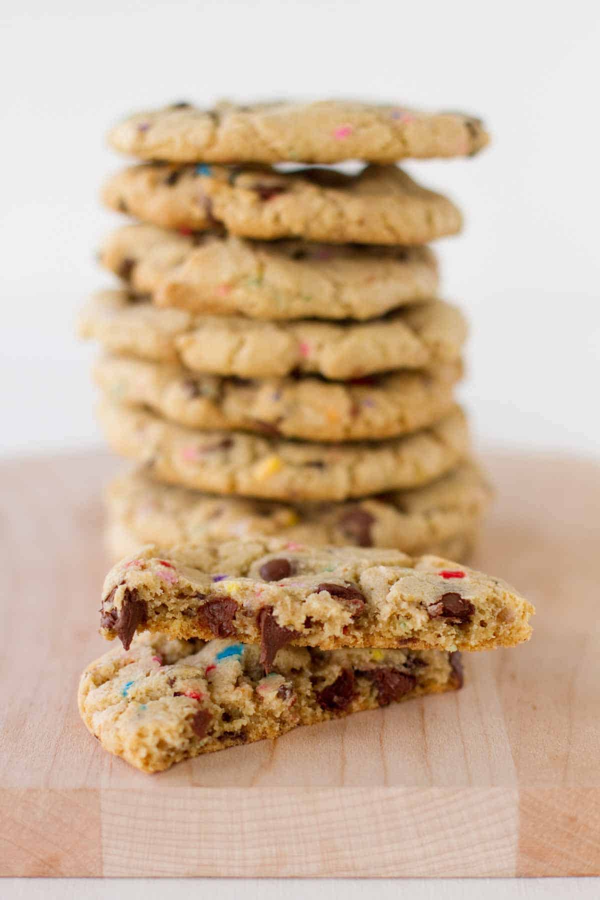 chocolate chip sprinkle cookie broken in half with stack of cookies behind