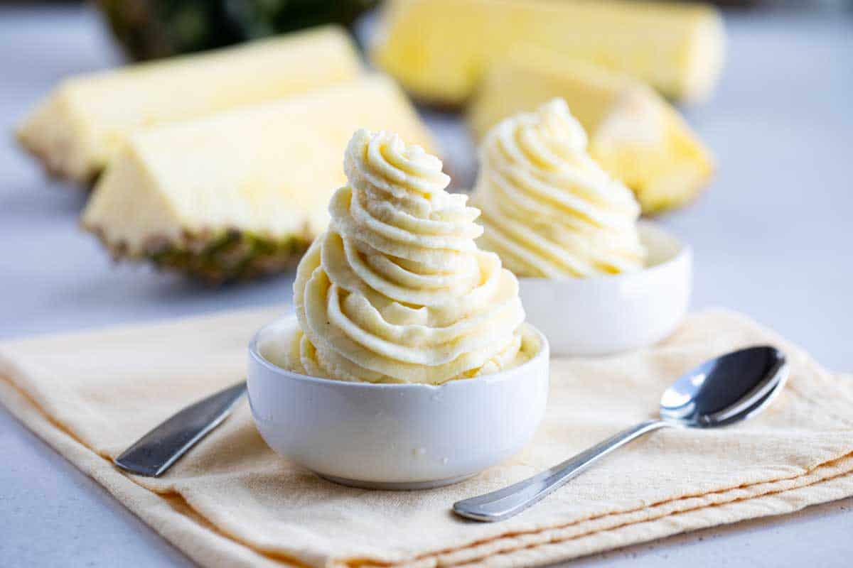 Missing the Disneyland classic? This homemade Pineapple Dole Whip Recipe is so simple, only takes 3 ingredients, and is done in less than 10 minutes! Pineapple Dole Whip Recipe in two small bowls with fresh pineapple
