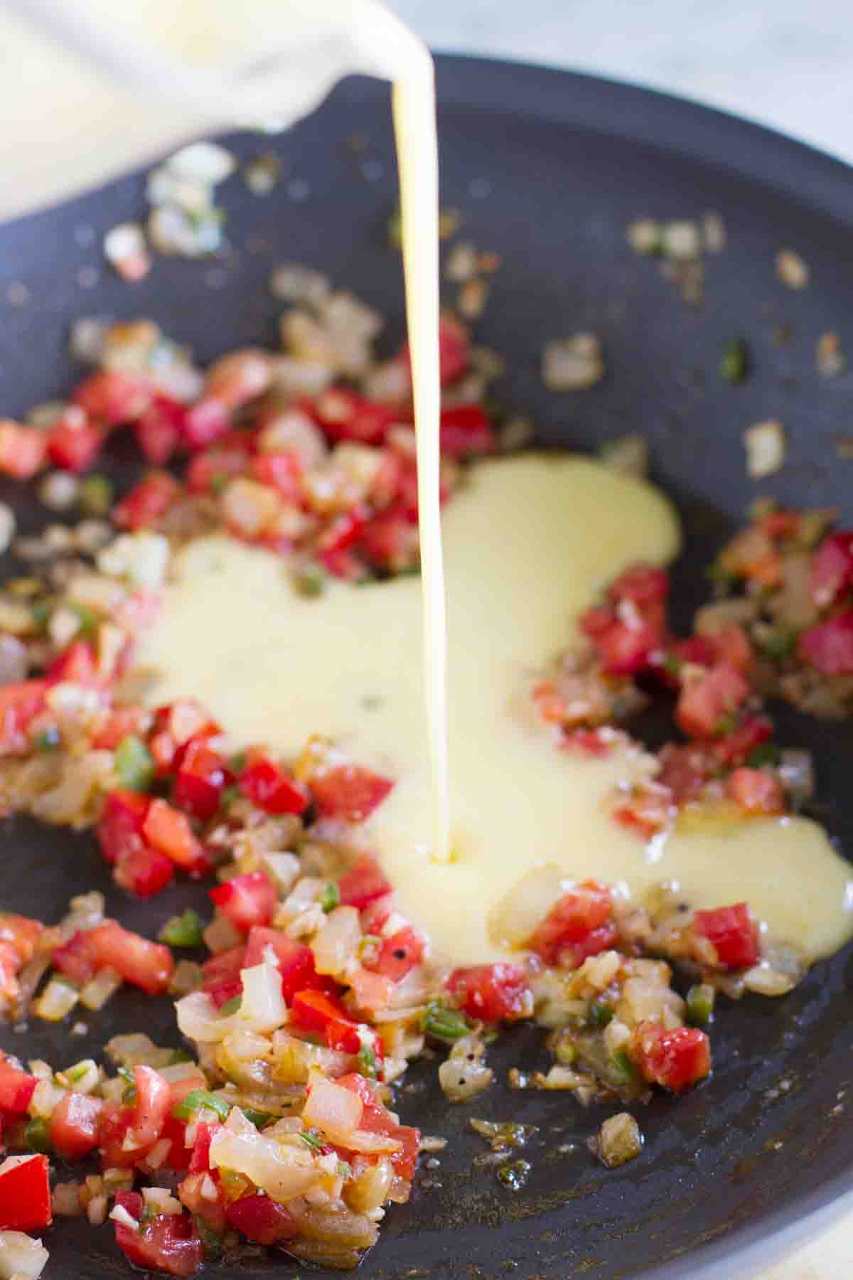 Eat your tacos for breakfast with these Migas Tacos filled with scrambled eggs with onions, jalapeños, tomatoes and crumbled tortilla chips. They are a great way to add a little Tex-Mex to your morning! Pouring eggs into sauteed tomatoes and onions