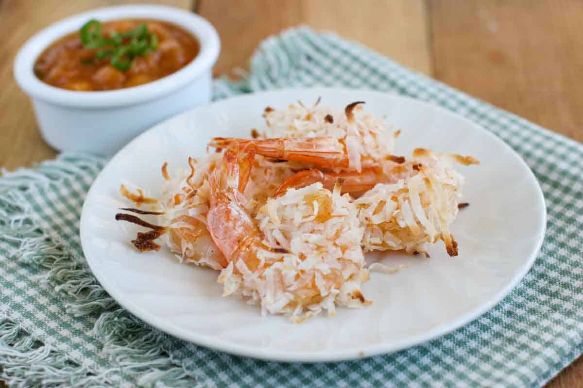 Love coconut shrimp but don't want to go to the hassle of frying? Try these Baked Coconut Shrimp that are served with a delicious Basil Peach Sauce. Baked Coconut Shrimp on a plate with basil peach dipping sauce behind.