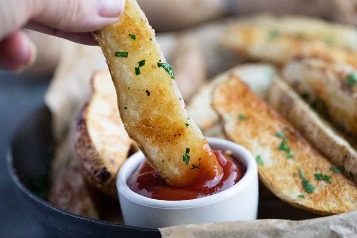 dipping a baked potato wedge into a small bowl of ketchup.