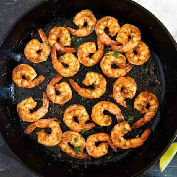 Cajun shrimp in a cast iron skillet with lime wedges.