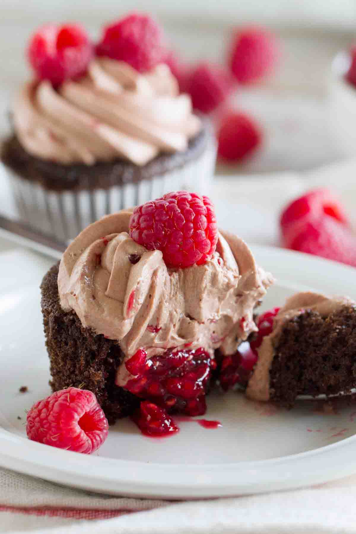 Chocolate cupcake topped with chocolate butterream broken in half to show raspberry filling.