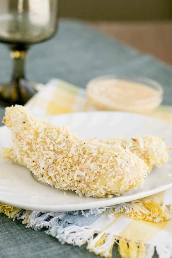 Coconut Chicken Tenders on a plate with creamy mango chutney in the back.