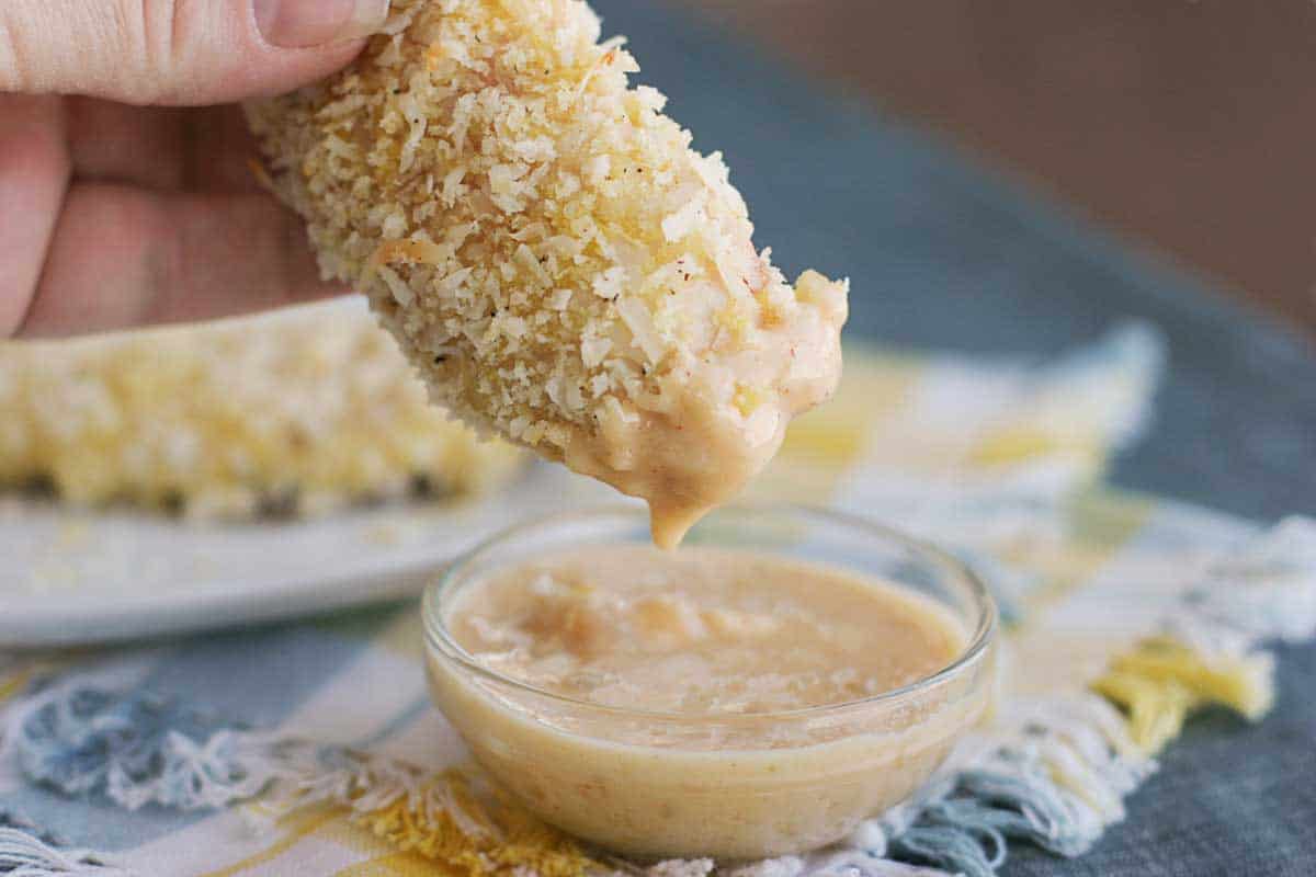 dipping a coconut chicken tender into creamy mango chutney