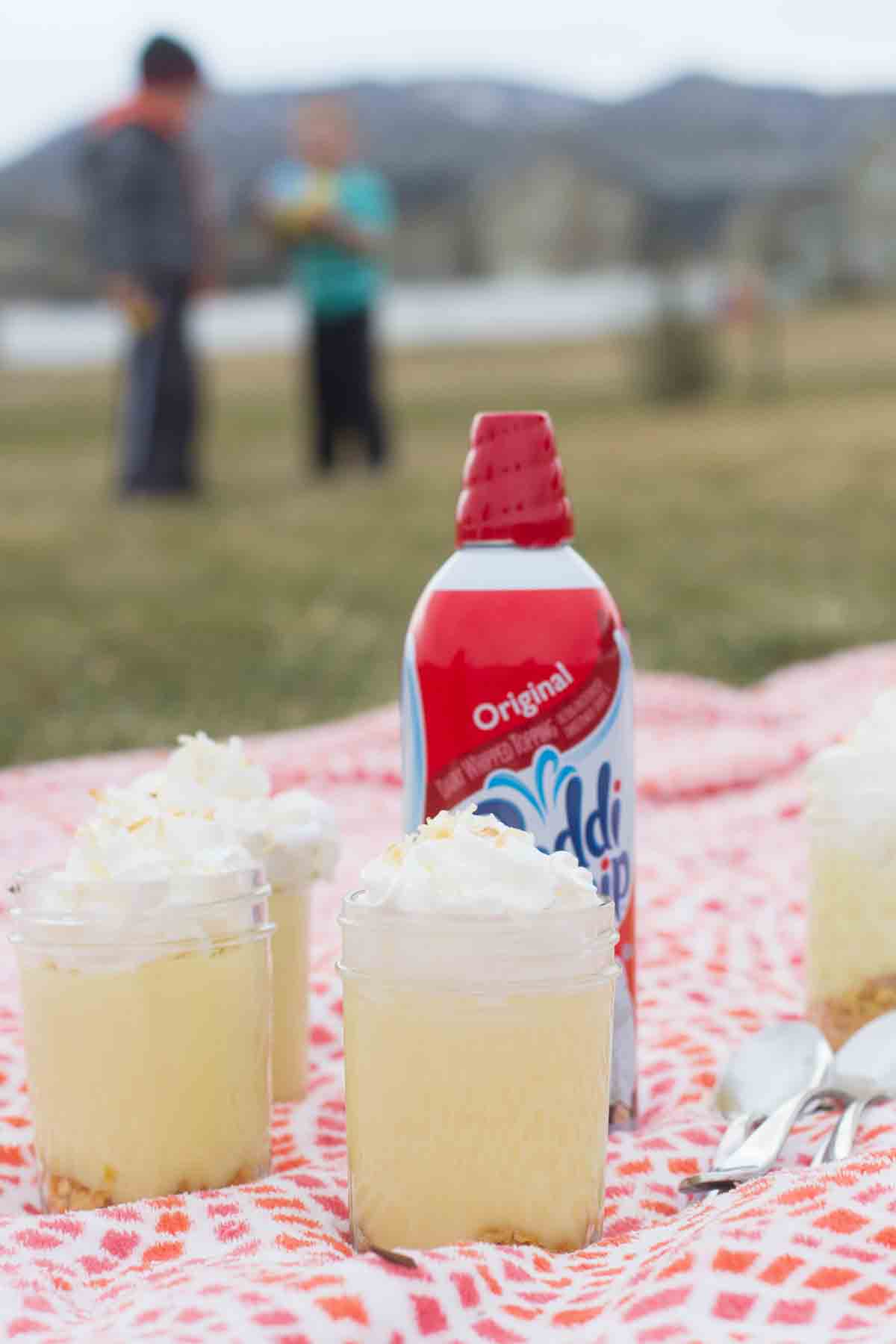 Jars of Coconut Lemon Pudding Parfait on a picnic blanket with a can of Reddi Wip.