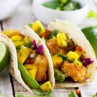 Two coconut shrimp tacos topped with mango salsa and avocado