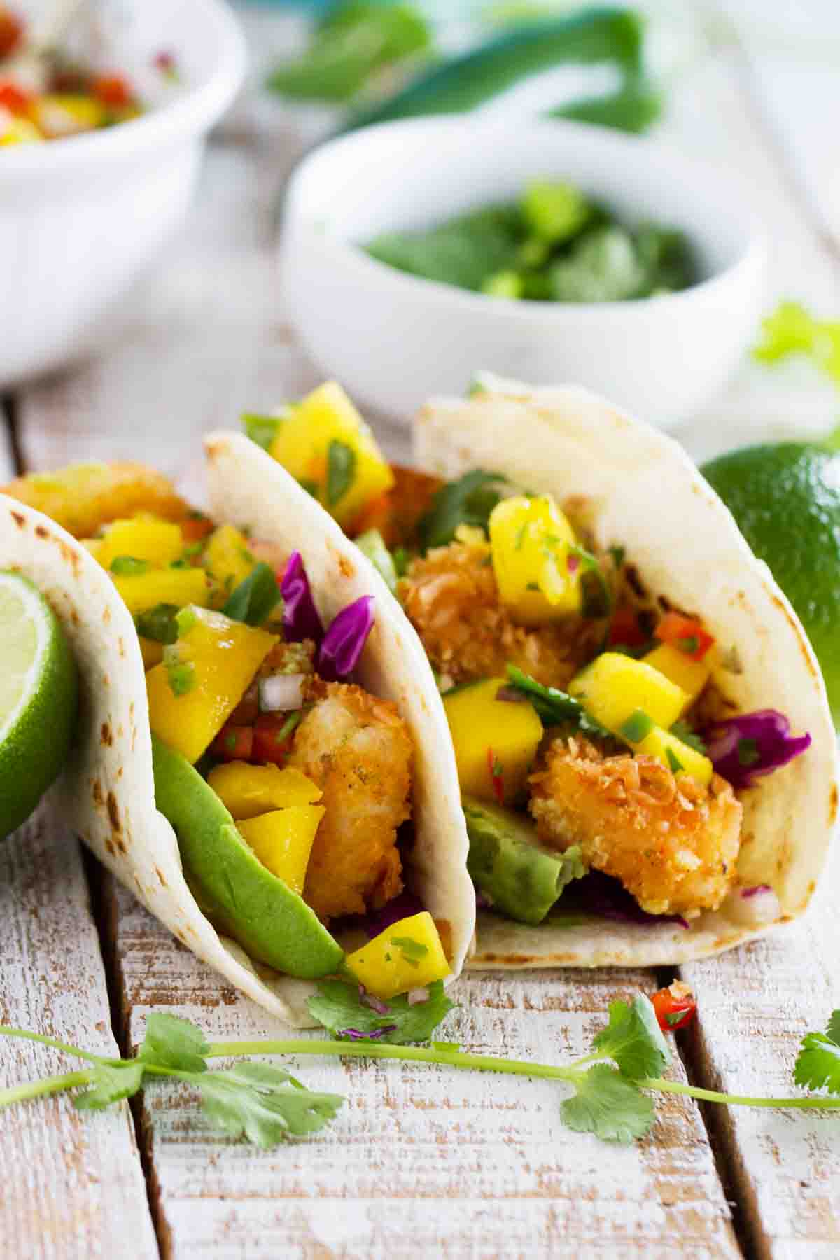 Two coconut shrimp tacos topped with mango salsa and avocado